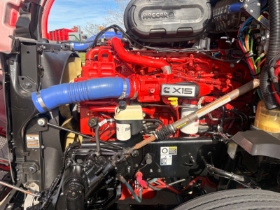 Kenworth T680 engine bay with red engine and blue radiator hose; visible labels include X15 badge on engine cover and various wiring harnesses.