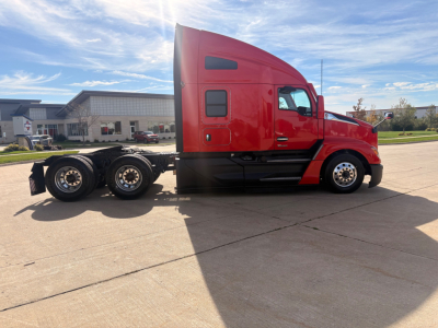 Kenworth T680 tractor side view in red, with sleeper cab and multiple wheels showing. No visible text readable on the side panels, no specific fluid labels.