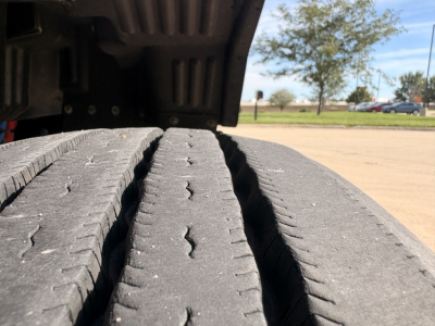 Kenworth T680 wheel tread close-up showing dual tires and undercarriage shadow in daylight.