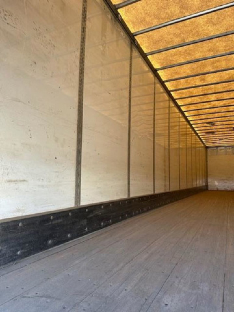 Interior of an empty van trailer showing wooden floor, side walls with metal ribs, and a yellowish translucent roof; no visible text.