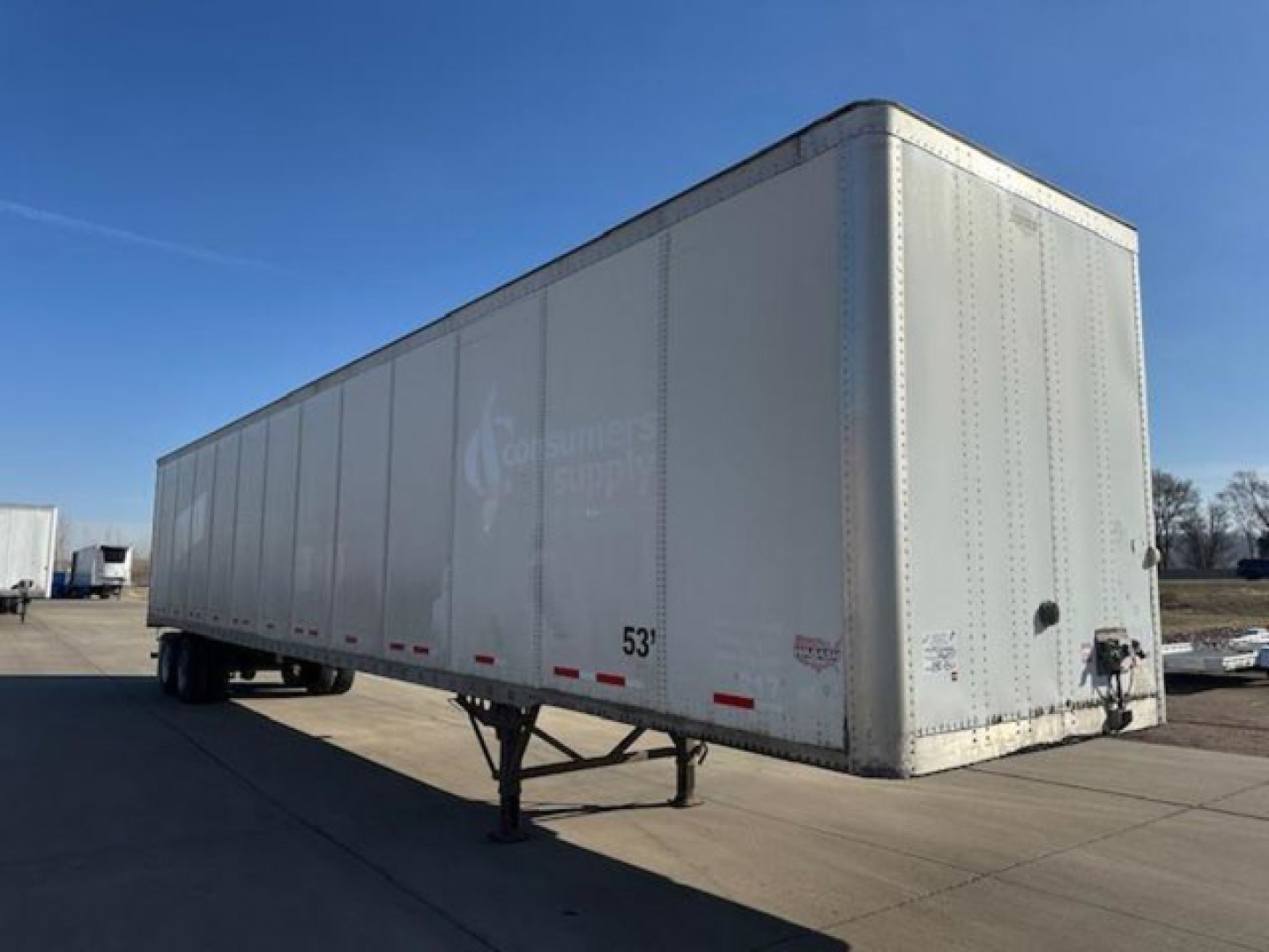 Trailer side and front showing a 53-foot dry van with landing gear and hitch; branding faint on white sides.