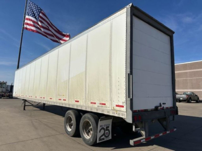 Trailer side and rear view of a 2013 Wabash van trailer showing dual rear wheels, white sided box with reflective tape, and American flag in background.