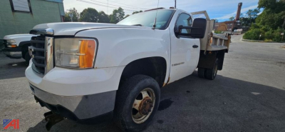 GMC Sierra 3500HD flatbed dump truck with plow, side view showing front grille, headlight, and dual rear wheels.