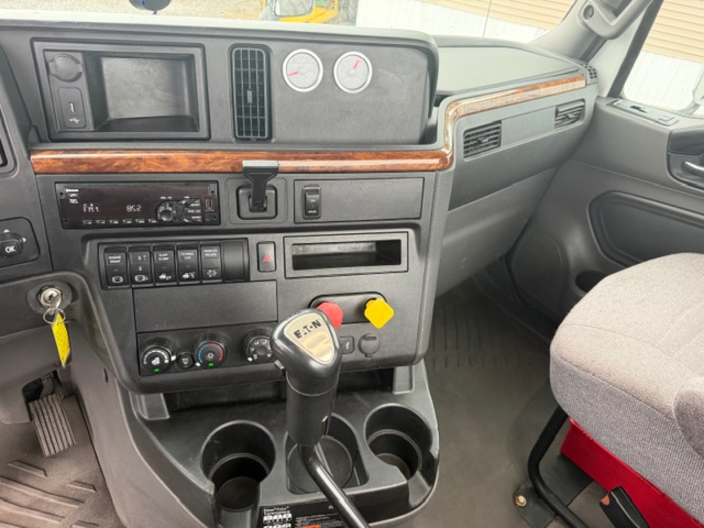 Truck cab interior showing steering column, dashboard gauges, gear shifter, cup holders, and wood trim on dash.