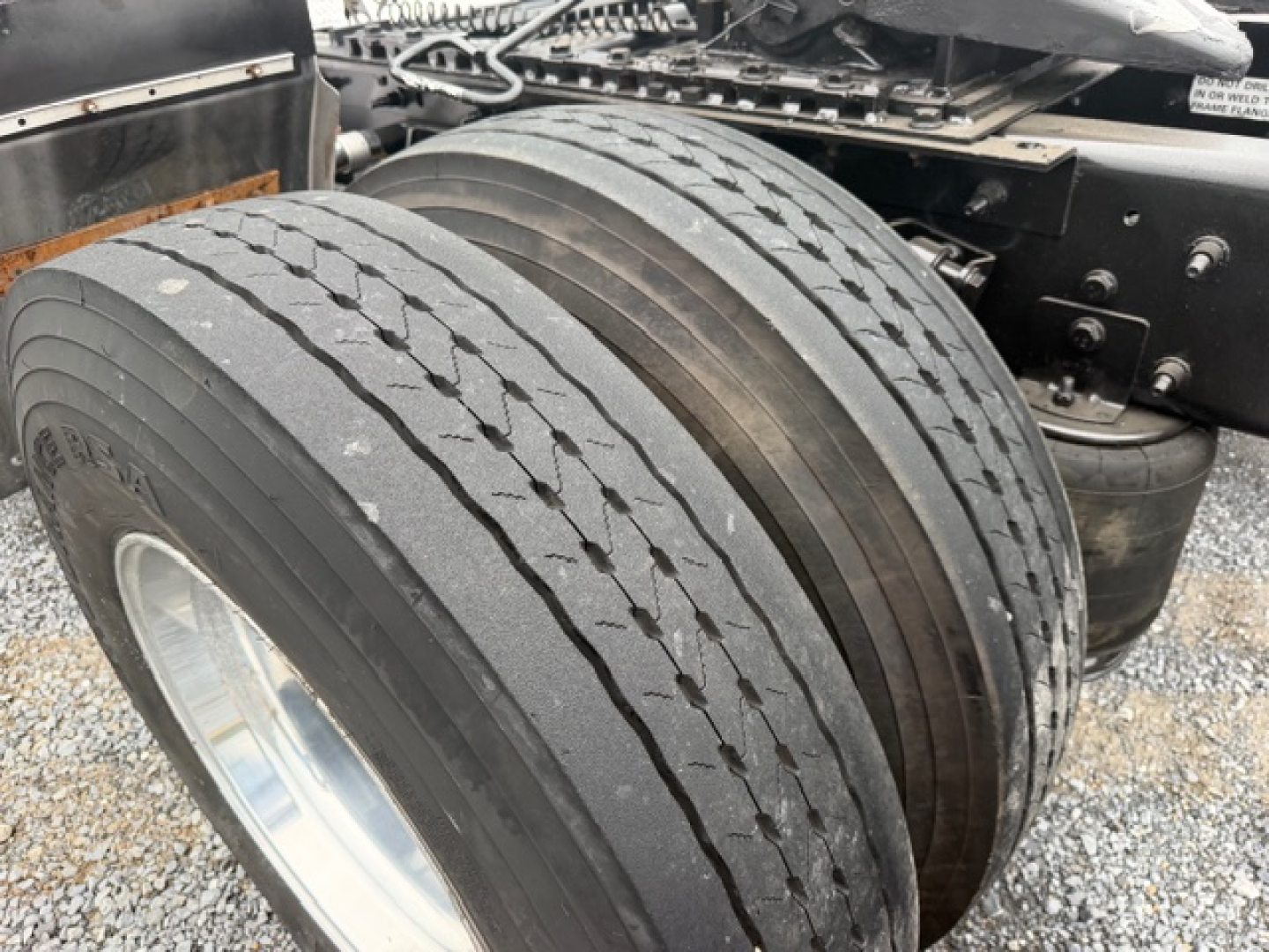 Truck axle with dual rear tires showing tread and wheel rims; part of International LT625 truck chassis visible in background.