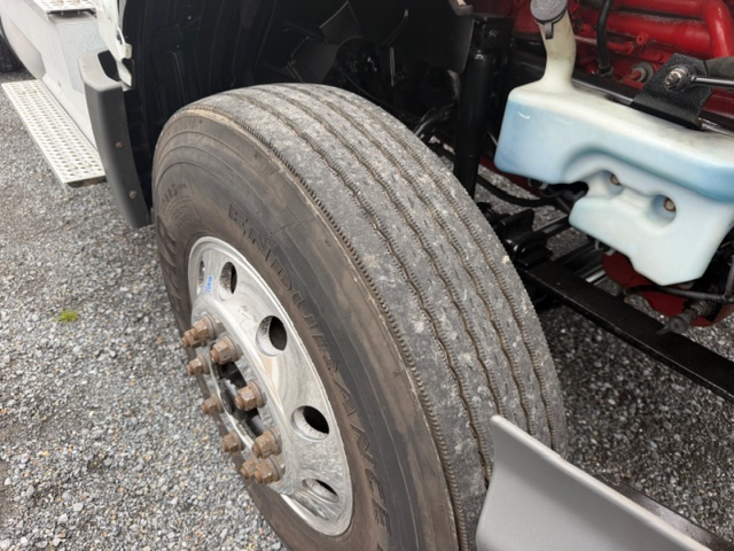 Truck wheel and front suspension area of an International LT625 cab, showing a large front tire, wheel hub, and engine bay components.