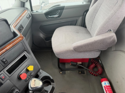 Cab interior of a 2018 International LT625 truck showing steering wheel, dashboard, and driver's seat with red portable seat mount and coiled air hose; part of dashboard with control knobs visible.