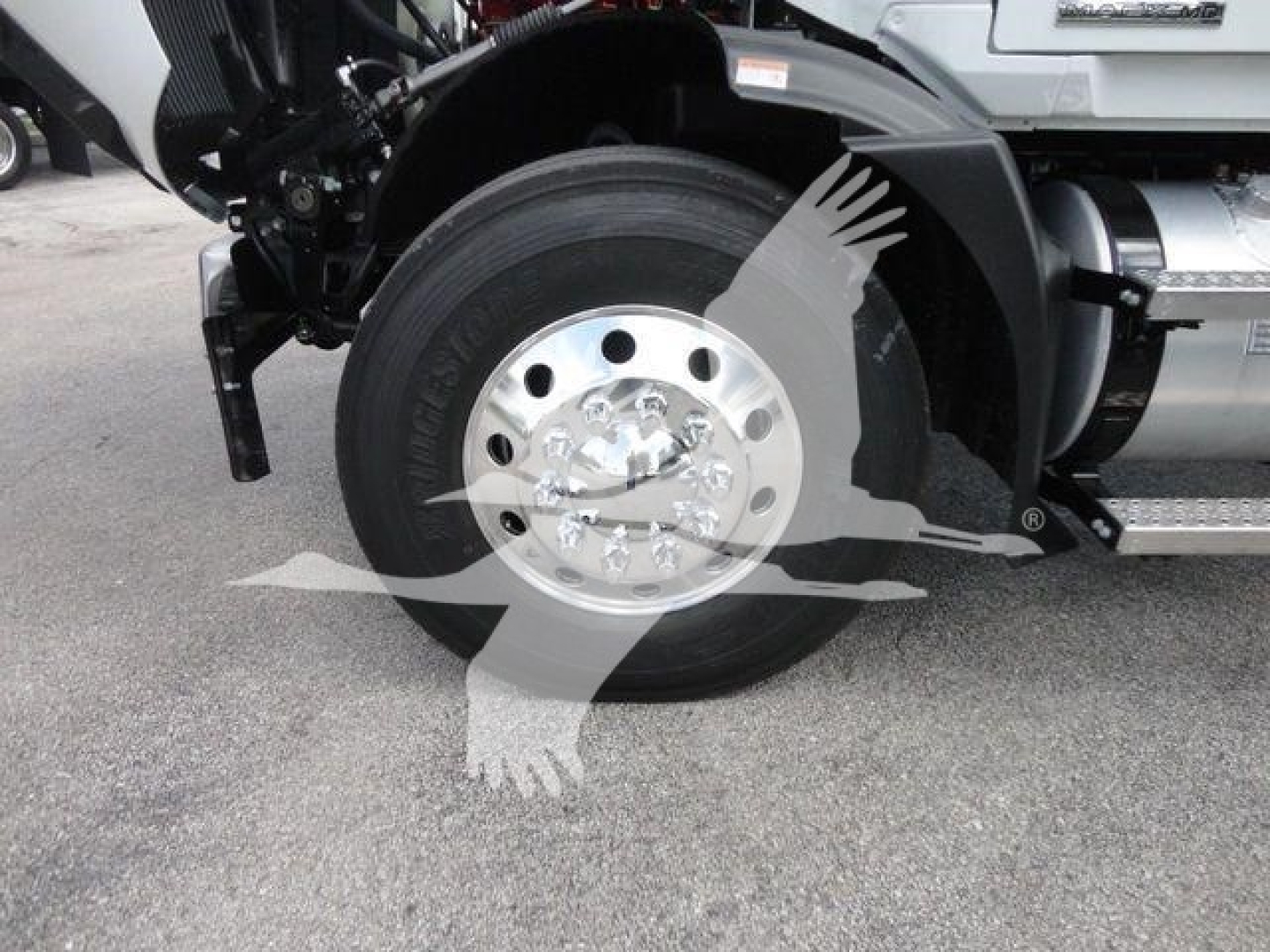 Cargo truck wheel and front suspension showing large steel wheel and hub with tire; part of Mack Md6 box truck cab visible.