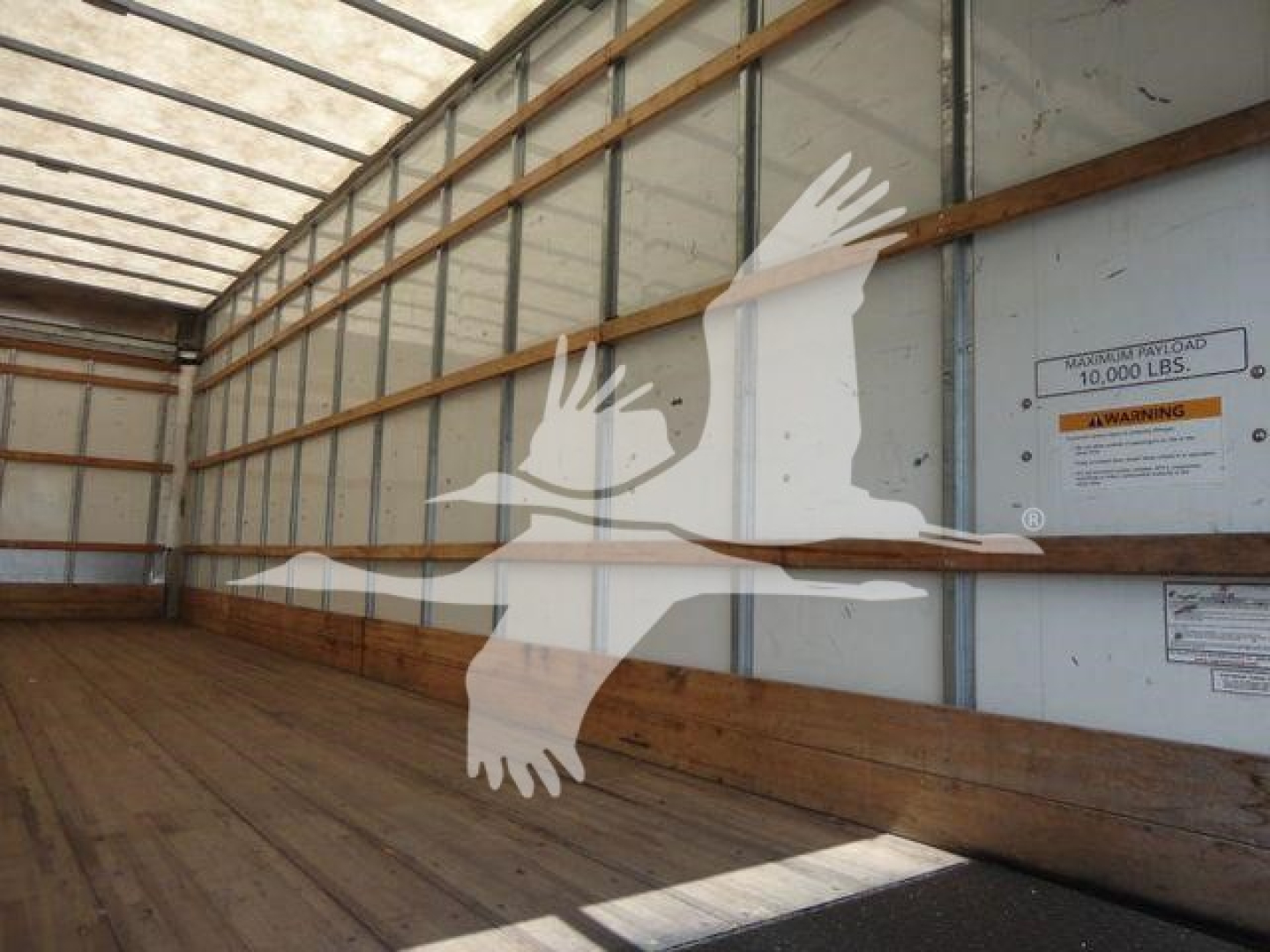 Box truck interior with white silhouette of birds overlaid; visible labels include 'MAX GROSS' and 'WARMING' on the side panel and a small sticker. Overall, a cargo trailer interior with wood floor and metal walls.