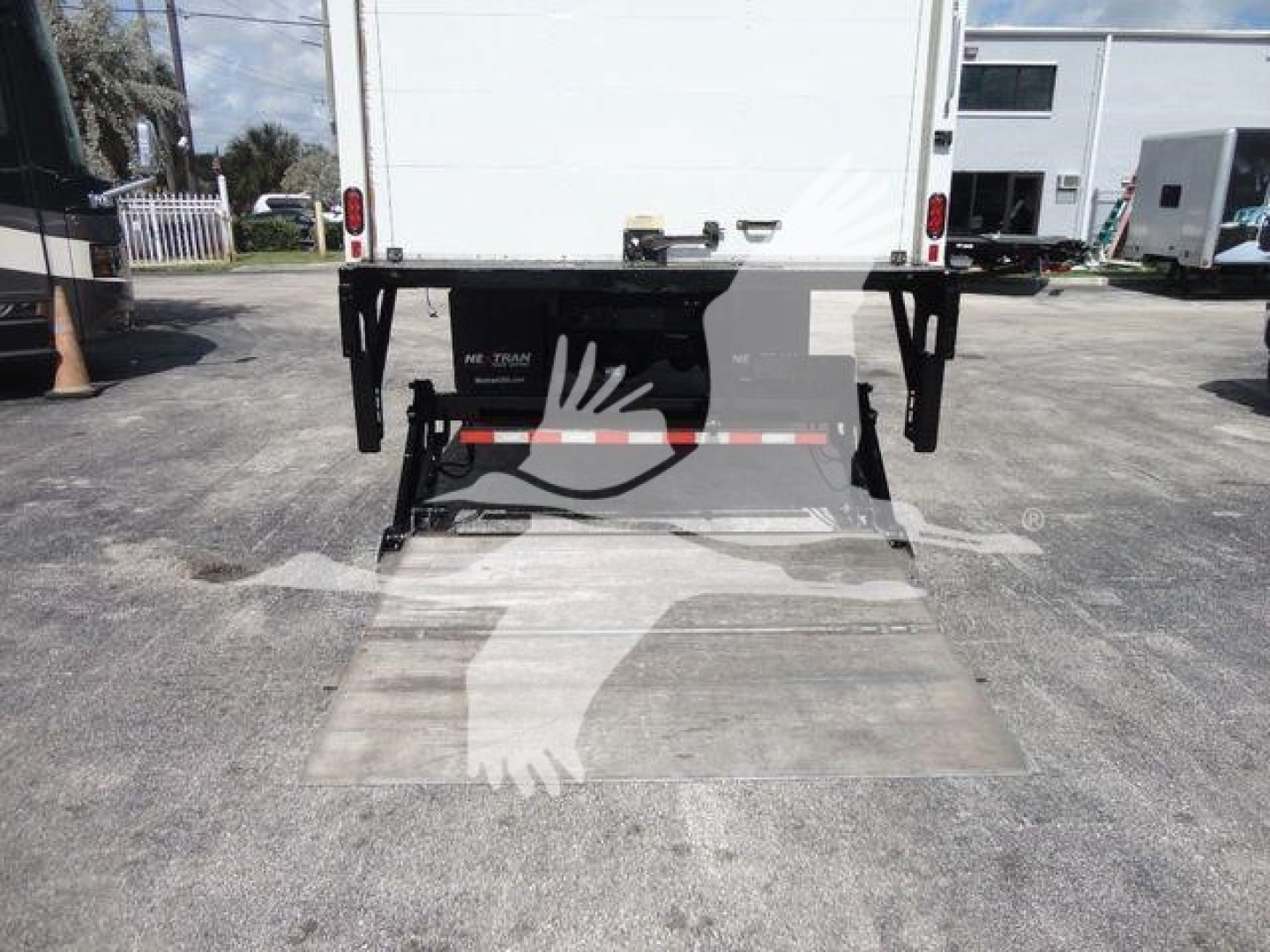 Box truck rear with ramp/ loading dock and hydraulic assembly visible under box on MACK MD6 stock unit, tail area and rear chassis components in view.