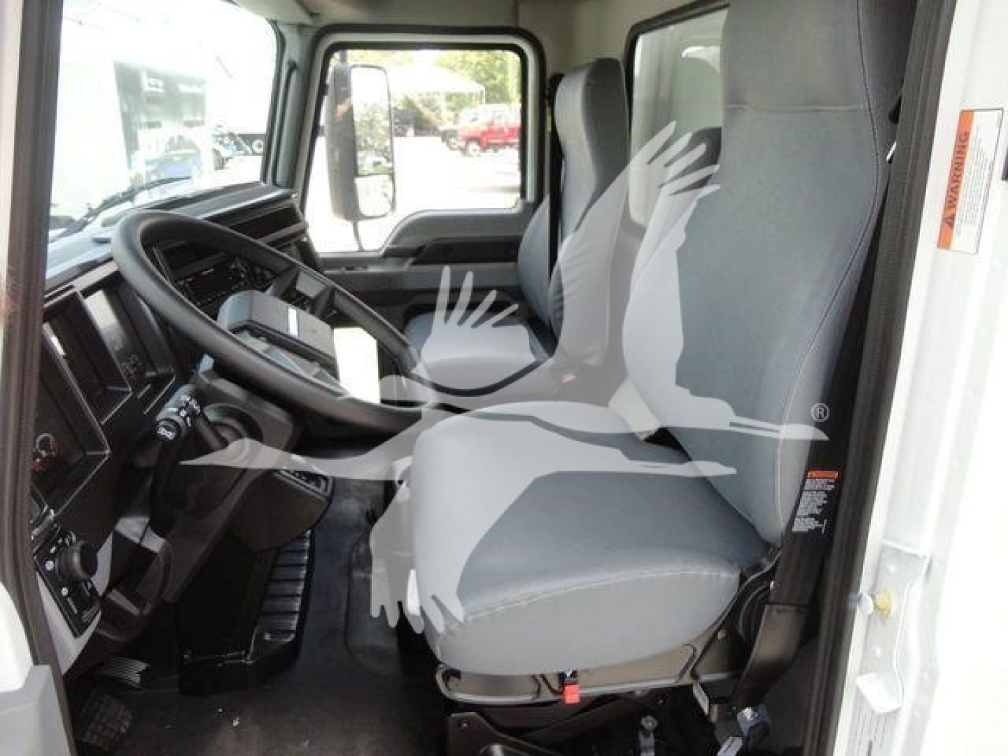 Mack MD6 cab interior showing driver seat and steering wheel; built-in dashboard and controls visible with front windshield and door window.