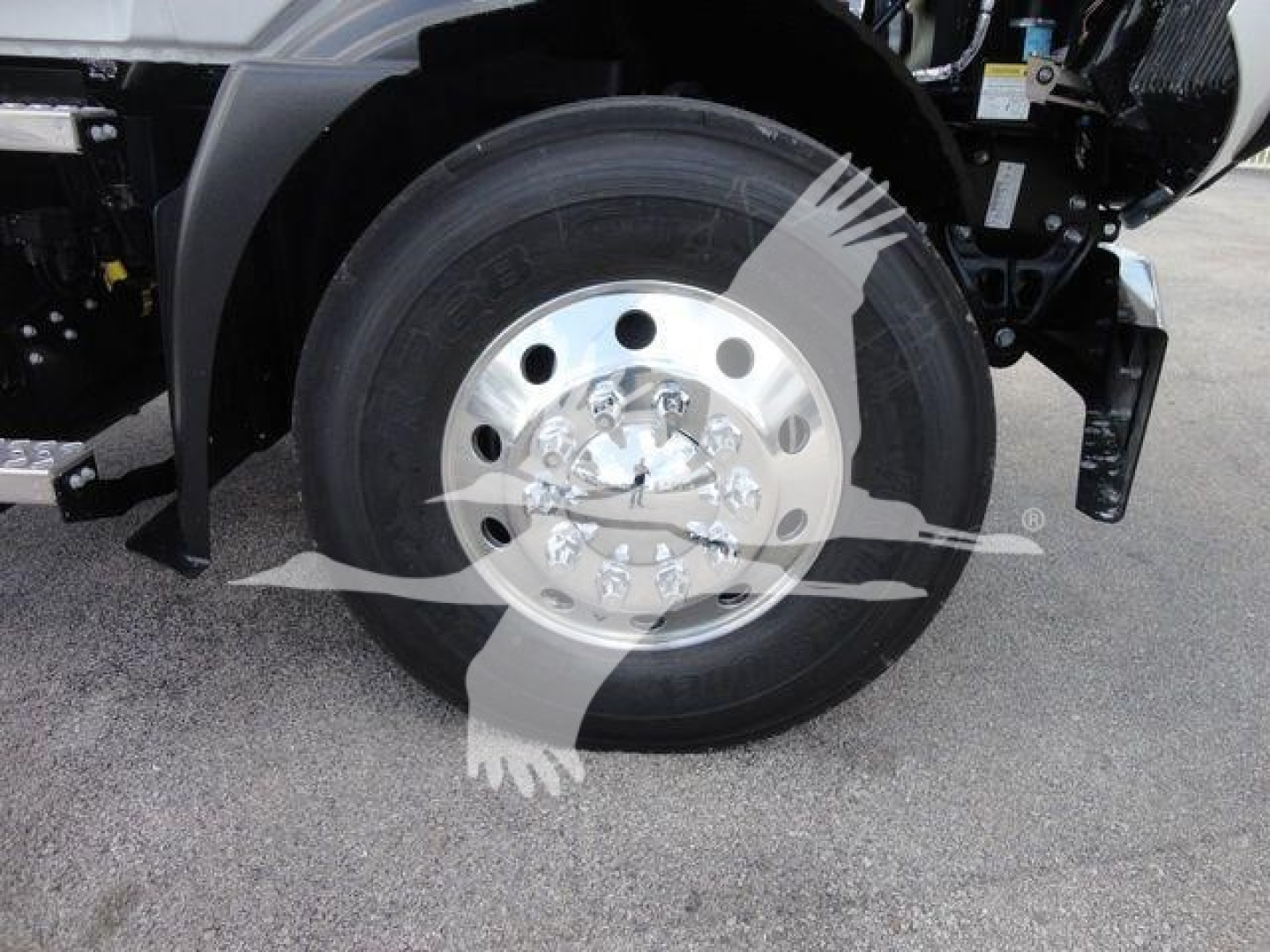 Front wheel and tire of a Mack Md6 truck showing steel wheel with multiple lug nuts and hub cover, part of the front suspension and fender in the frame.