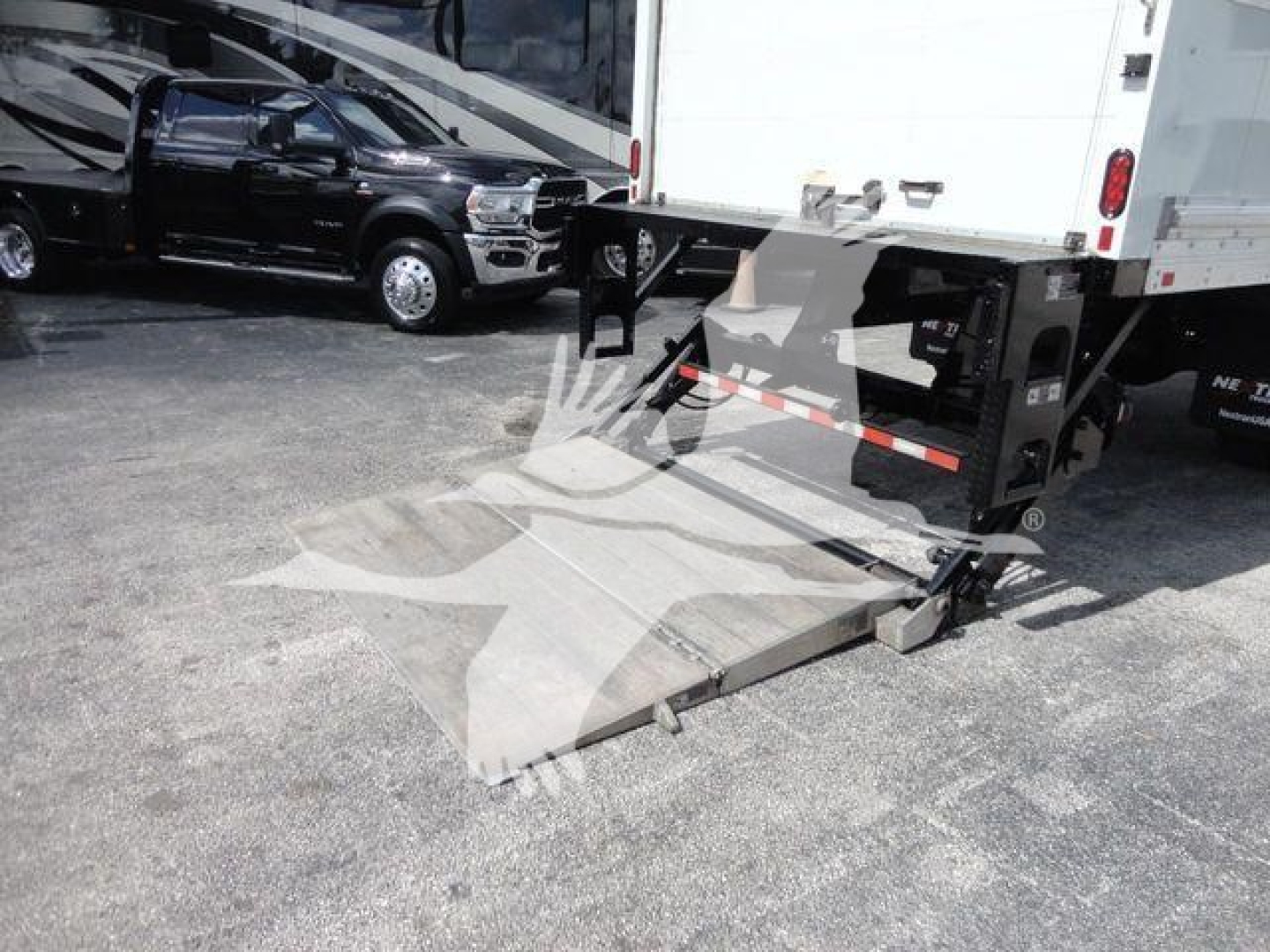 Truck with rear liftgate ramp extended showing box truck undercarriage and loading platform.