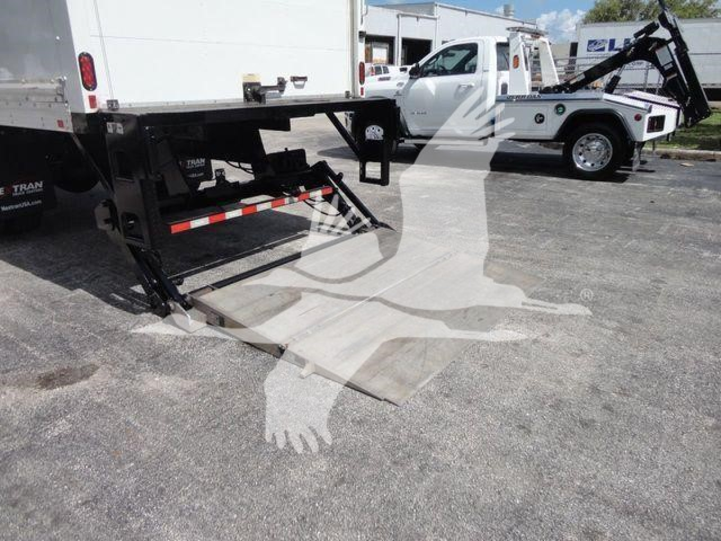 MD6 truck bed with hydraulic lift gate and loading ramp visible, White Mack MD6 box truck in background.