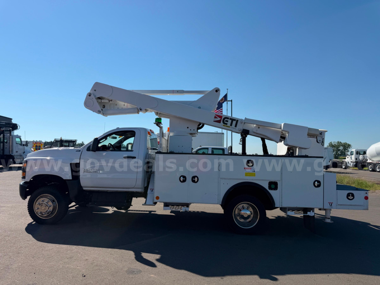 Truck-mounted bucket lift utility body on a Chevrolet Silverado 6500HD service vehicle with boom extended, side view showing utility compartments and cross-braced arm.