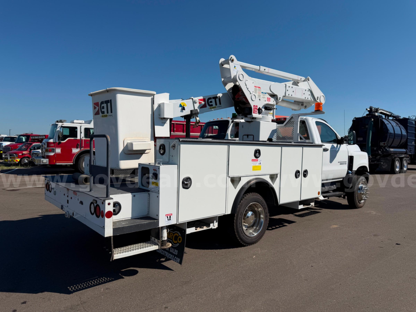 Utility bucket truck with boom crane and service compartments in an outdoor lot.
