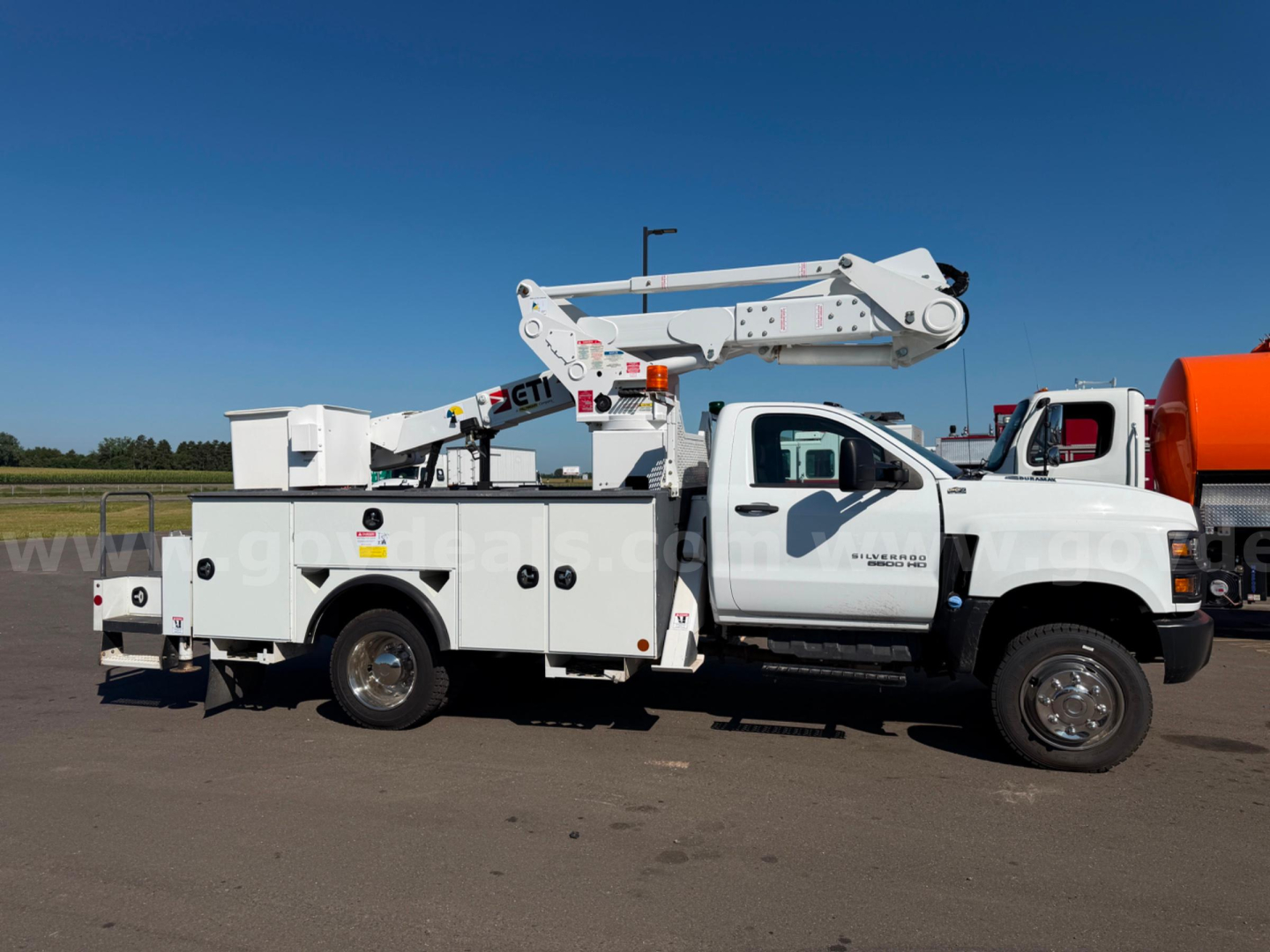 Truck bed utility body with bucket lift on Chevrolet Silverado 6500HD in-service, side view showing bucket platform and crane hardware.