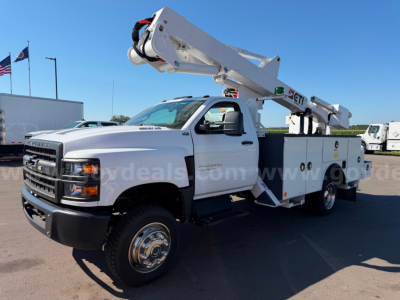 Front three-quarter view of a white 2020 Chevrolet Silverado 6500HD bucket truck with boom elevated, utility compartments along the side, dual rear wheels, and a black front bumper.