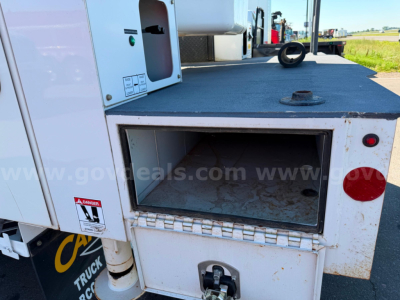 Truck equipment bay showing open rectangular storage compartment on a 2020 Chevrolet Silverado 6500HD utility bed with warning label and textured step surface.