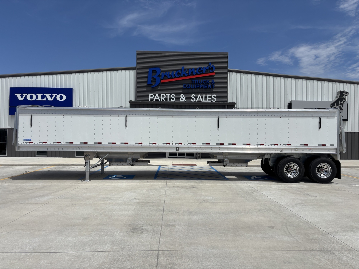 Semi trailer in a dealership lot showing a 42' aluminum grain hopper trailer with 68" sides, dual rear axles, and Volvo/Buckner Parts signage in the background.