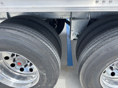 Trailer axle area showing dual rear tires with polished rims and a blue center seam in the gap between wheels under a metal frame.