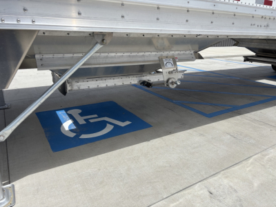 Underbody of new 2027 Stoughton 42' aluminum grain hopper trailer with accessibility sign on the concrete. A hitch and support braces visible.