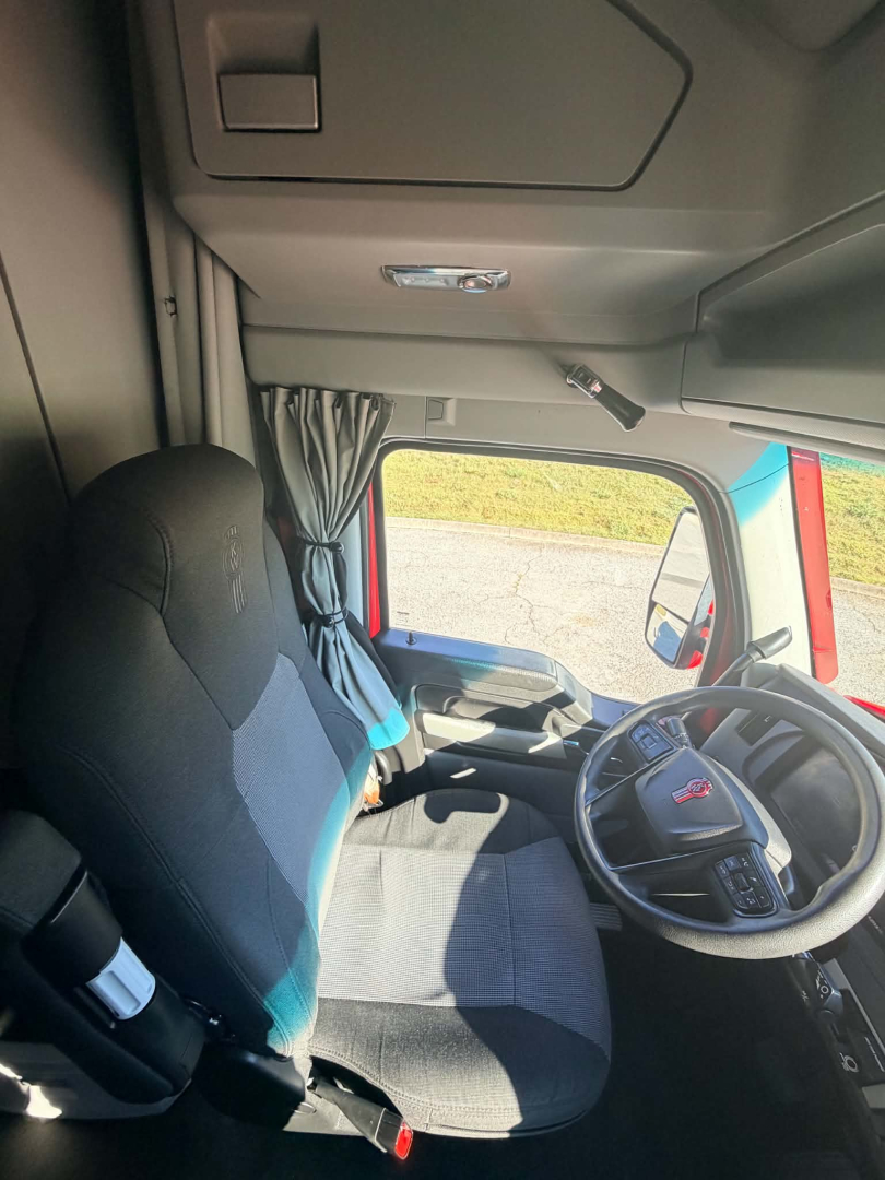 Truck cab interior of a 2023 Kenworth T680 with steering wheel, driver seat, and overhead console visible