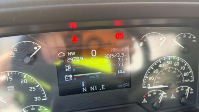 Kenworth T680 dash display shows digital gauges with NW 12978.9 miles, zero miles, MPG 0, and various warning icons; center screen displays 7802? 301523.3 L?; letters N N I E beneath; multiple gauge dials on sides.