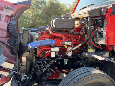 Kenworth T680 engine bay showing red Cummins X15 engine with blue hoses and surrounding components.
