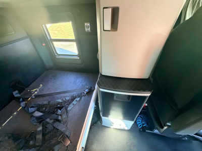 Kenworth T680 sleeper cab interior showing storage cabinet and seat area, with window and seat belt visible.