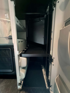 Kenworth T680 cab interior showing vertical storage shelves and an open fridge/freezer area with metal shelving.