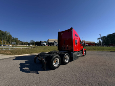 Kenworth T680 tractor with red sleeper cab, rear view showing fifth wheel and dual rear axles, in a parking lot.