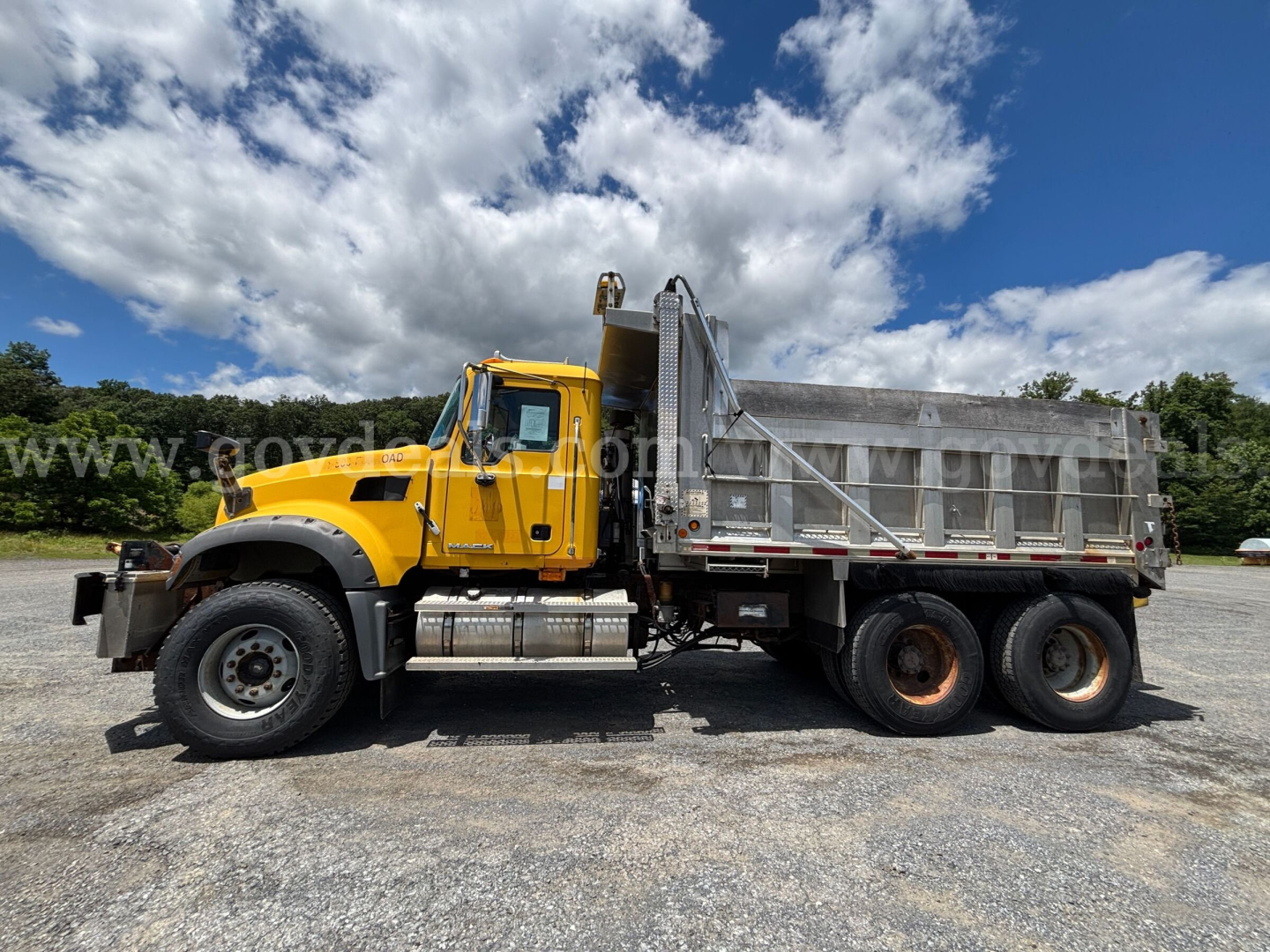 Dump truck side view showing 2008 Mack GU713 with yellow cab and gray dump bed.