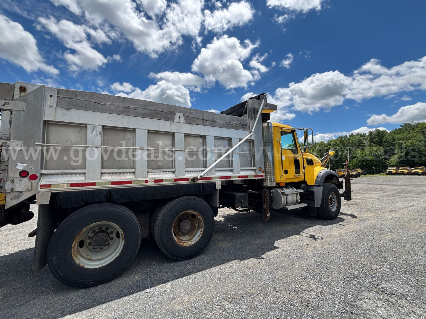 Dump truck side view showing yellow cab and large gray dump bed on a Mack GU713 with three rear axles.
