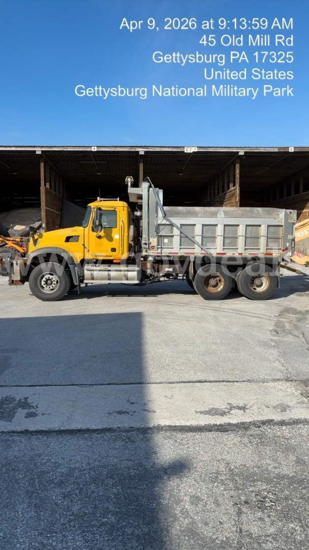 Mack GU713 dump truck side view showing yellow cab and gray dump bed with text watermark in upper area.