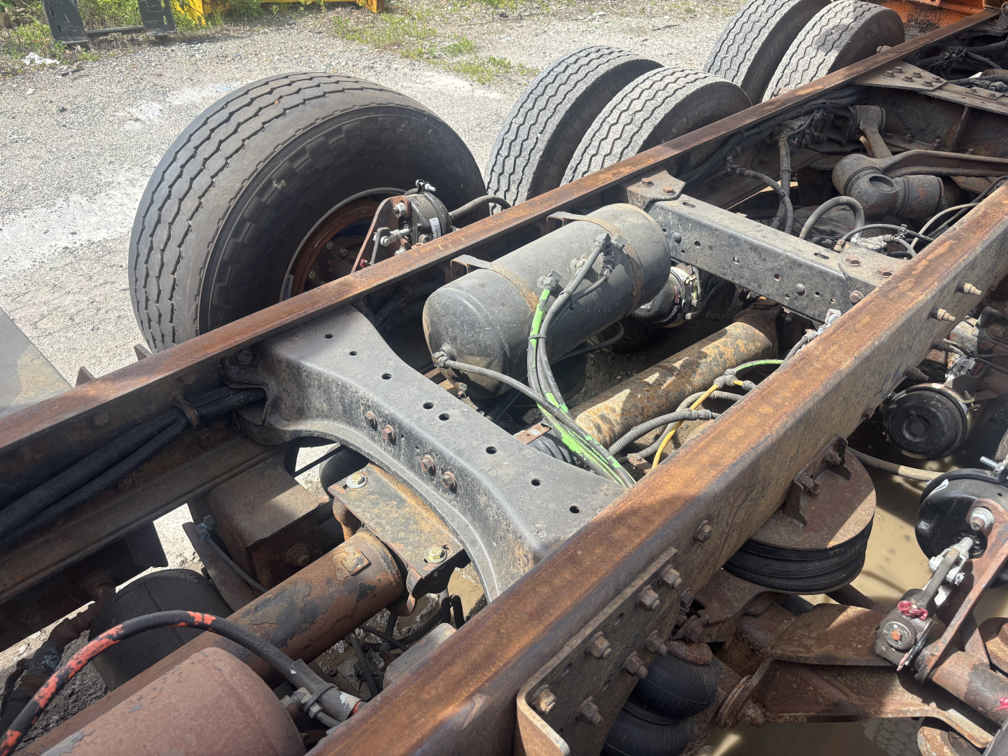 Kenworth T880 chassis showing dual rear axles, frame rails, air lines, and suspension components with rust and wear.