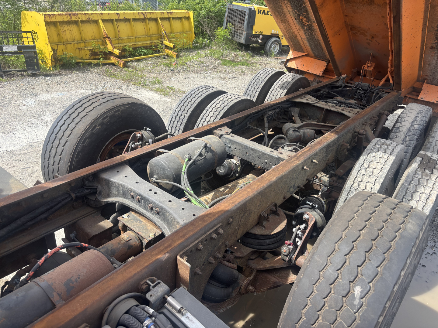 Dump truck chassis with dual rear axles and fifth wheel, exposed frame and suspension components, Kenworth T880 undercarriage view.