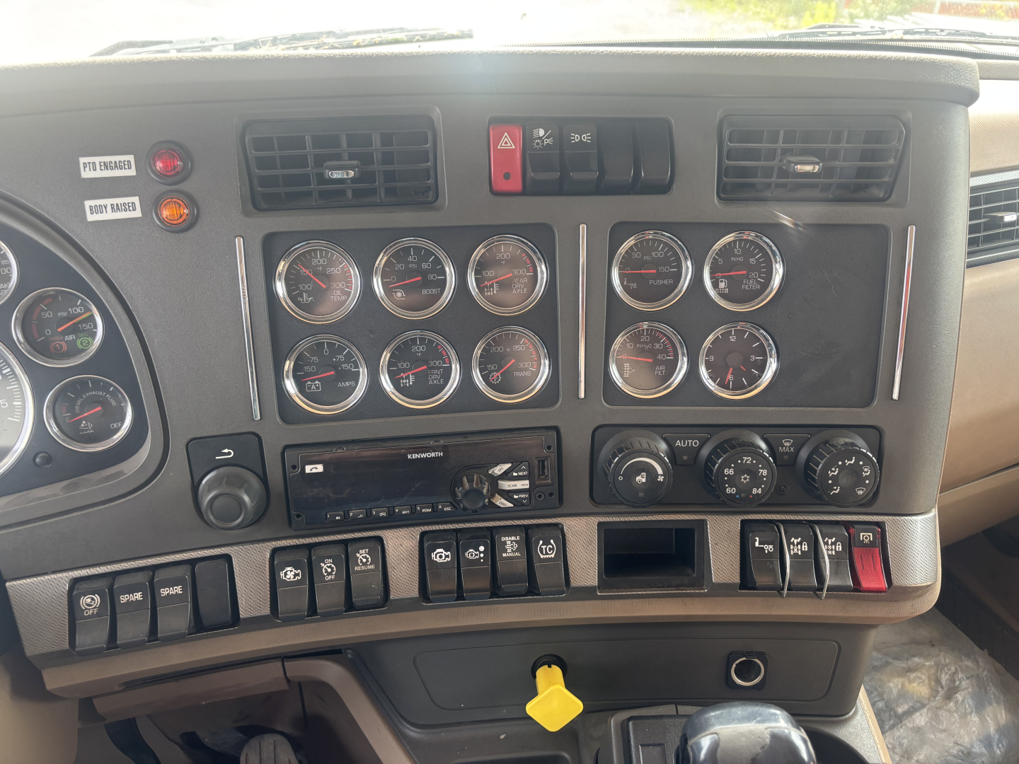 Kenworth T880 dashboard showing multiple gauges and control switches, center console with hazard switch, climate controls, and a yellow key in the ignition area.