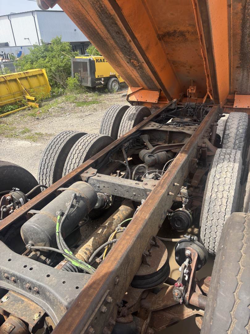Kenworth T880 chassis view with the dump bed raised showing drivetrain, suspension, and dual rear axles with visible hoses and components.
