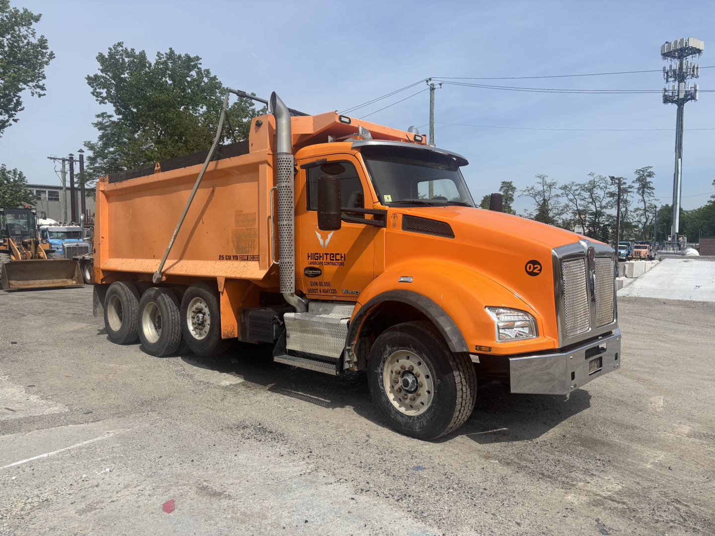 Kenworth T880 dump truck in orange showing side view with payload bed and rear dual wheels, Kenworth emblem on grille, company logo ‘HighTech…’ on door, VIN not readable.