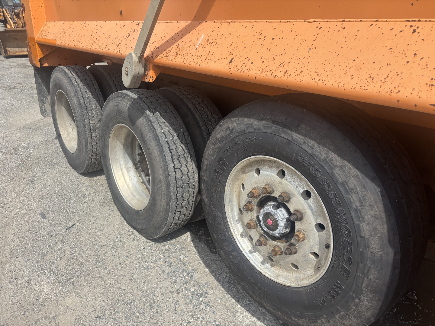Kenworth T880 dump truck wheel end showing tandem axles and heavy-duty tires with rim, orange dump bed side visible.