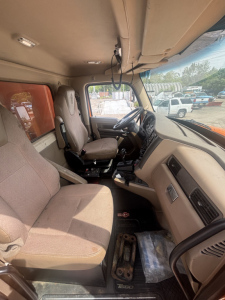 Cab interior of a 2016 Kenworth T880 dump truck showing tan fabric seats, steering wheel, dashboard, and floor with metal pedal area.