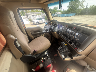 Cab interior of a 2016 Kenworth T880 dump truck showing driver seat, dashboard with multiple round gauges, steering wheel, gear shifter, and control panels.
