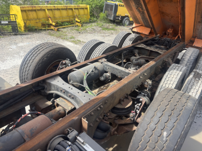 Dump truck chassis with dual rear axles and fifth wheel, exposed frame and suspension components, Kenworth T880 undercarriage view.