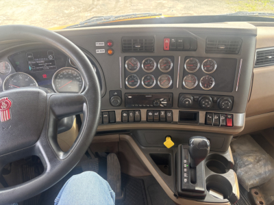 Kenworth T880 cockpit showing steering wheel, instrument cluster, multiple gauges, gear shifter, and dashboard switches.