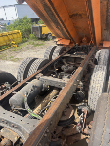 Kenworth T880 chassis view with the dump bed raised showing drivetrain, suspension, and dual rear axles with visible hoses and components.