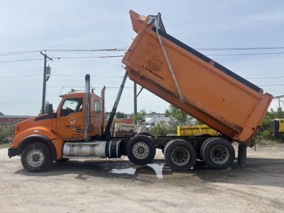 Kenworth T880 dump truck in service, orange cab and dump bed raised, side view with multiple axles, some text on cab doors.