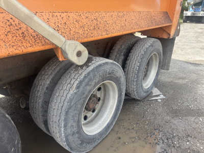 Dump truck wheels and lower body of a 2016 Kenworth T880 dump truck showing dual rear axle tires and orange cargo bed.