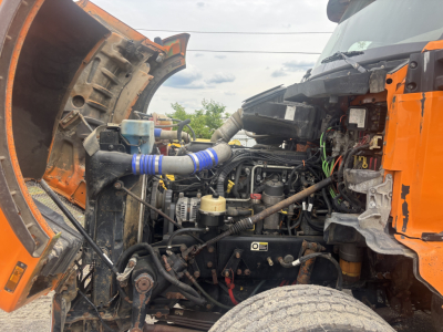 Engine bay of a 2016 Kenworth T880 dump truck showing exposed engine components, hoses, and wiring with orange body panels.