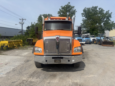 Kenworth T880 dump truck front view showing large mesh grille and orange cab with chrome bumper.